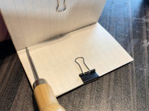 An awl poking holes in the spine of the mini journal