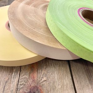Three large rolls of vintage teletype tape in yellow, beige, and lime green