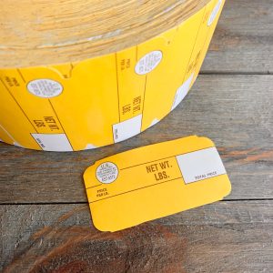 A large roll of yellow vintage butcher price labels with a label laid out next to it showing the brown text