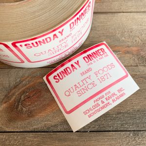 A large roll of white & red butcher label stickers for a Sunday Dinner, plus a separate label laid flat on the surface