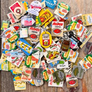 A large pile of colorful vintage food-themed Dutch advertising pins-turned-charms with silver jump rings
